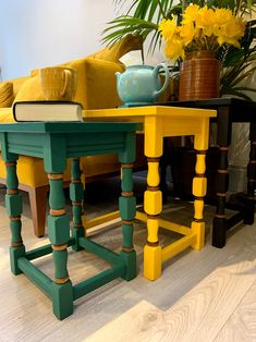 two tables painted yellow and green with vases on them in front of a couch