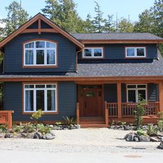 a blue house with white windows and wood trimmings on the front, surrounded by trees