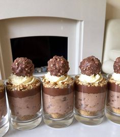 four desserts are arranged in small glasses on a table with a fireplace behind them