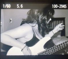 black and white photograph of a woman playing a bass guitar with her hands on the strings