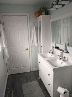 a white bathroom with two sinks and towels on the rack above it's door