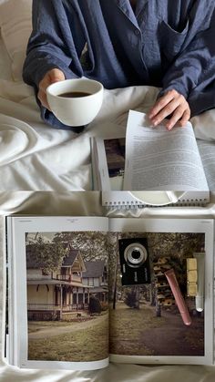 a person sitting on a bed with an open book and cup of coffee in front of them