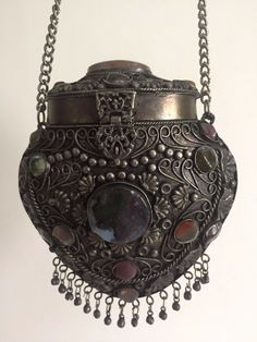 THIS VINTAGE 1960'S HANDCRAFTED TIBETAN METAL & SEMI PRECIOUS STONES CROSS BODY ORNATE EVENING BAG IS A VERY SPECIAL AND UNIQUE PIECE TO ADD TO YOUR COLLECTION. THE ETHNIC BOHO STYLE OF THIS SMALL SCALE HANDCRAFTED CAST METAL EVENING HANDBAG FEATURES A HINGED TOP LID, A BLACK VELVET LINING, INTRICATE FLORAL RELIEF METAL PATTERNING, ASSORTED MULTI COLOR INSET SEMI PRECIOUS GEMSTONES, BOTTOM EDGE METAL BALL FRINGE & A METAL CHAIN LINK SHOULDER STRAP. THE ELEGANT AND EXOTIC EVENING BAG HAS A SMALL Vintage Beaded Purse, Vintage Beaded Bag, Medieval Antiques, Whimsigoth Bag, 1800s Accessories, Dnd Bag, Vintage Market Booth, Witchy Gifts