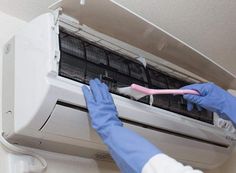 a person in blue gloves is cleaning an air conditioner with a pink toothbrush