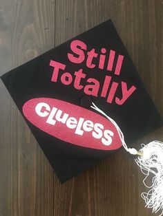 a graduation cap with the words still totally clueless on it sitting on top of a wooden table