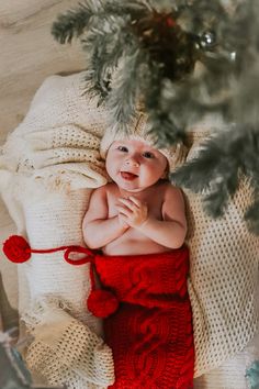 a baby in a red dress laying on top of a blanket next to a christmas tree