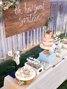 an outdoor dessert table with cake, cupcakes and other treats on it in front of a wooden sign that says oh how sweet sixteen