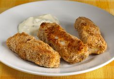 three pieces of chicken on a white plate with ranch dressing in the background and a yellow table cloth