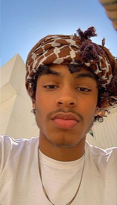 a young man wearing a white t - shirt and a brown patterned headwrap