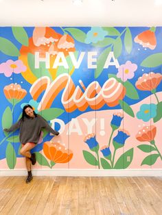 a woman standing in front of a colorful wall with flowers and words painted on it