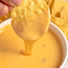 a person dipping cheese into a bowl of dip with crackers in the back ground