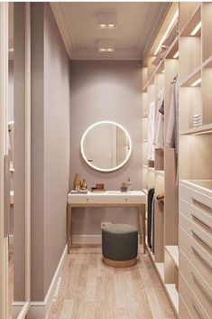 a walk - in closet with white drawers and wooden flooring, lighted by round mirrors