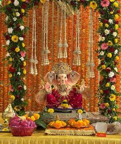 an elephant statue sitting on top of a table covered in flowers and decorations with bells hanging from the ceiling