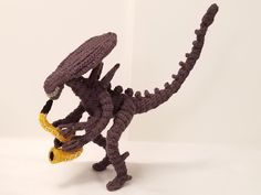 a crocheted toy dinosaur with a yellow bell on its neck and tail, standing upright in front of a white background