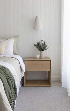 a bed sitting next to a nightstand with a plant on it