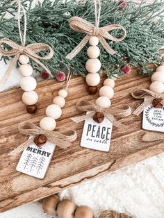 wooden beaded ornaments are hanging on a wood board with ribbon and tags that say peace