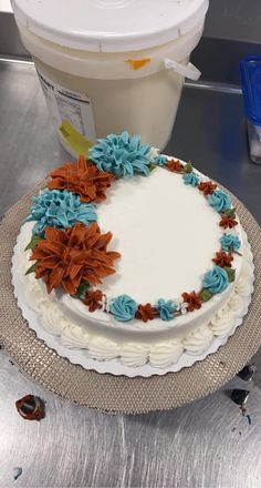 a white cake with blue and orange flowers on it next to a container of yogurt