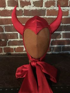 a red devil mask with horns on it's head is shown in front of a brick wall