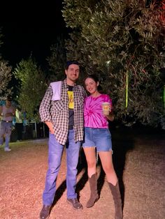 a man and woman standing next to each other in front of an olive tree at night