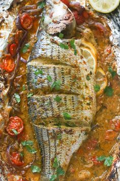 grilled fish on foil with tomatoes, lemons and parsley garnish