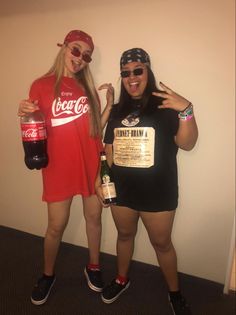 two women standing next to each other in front of a wall with coca cola bottles