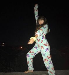 a woman in pajamas is doing yoga outside at night with her arms up and legs spread out