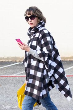 a woman is walking and looking at her cell phone while wearing a black and white checkered ponchard