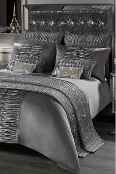 a bed with silver sheets and pillows in a black room at night, surrounded by lights