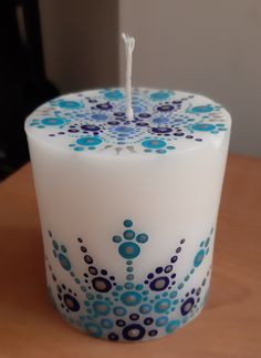 a white candle with blue and purple designs on it sitting on a table next to a black cat