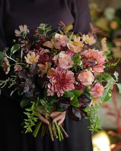 a woman holding a bouquet of flowers in her hands and wearing a black dress with dark sleeves