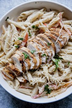 a white bowl filled with pasta and chicken on top of a blue countertop next to a fork