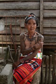 an old woman with tattoos sitting on a bench