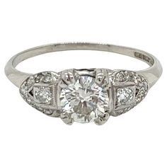 A true classic from the Art Deco era, this platinum ring exudes timeless elegance. The centerpiece is a modern round brilliant diamond weighing approximately 0.65 carats. This dazzling diamond exhibits an enticing H color and bright SI1 clarity. Rather than sitting high, the diamond sits just 4.3mm high off the finger in an intricate filigree setting. Flanking each side of the center diamond is a sparkling semi-circle design comprised of 8 single cut and full cut accent diamonds. These supplemental diamonds total approximately 0.20 carats and frame the center stone in perfect geometric symmetry. The ornate setting measures 6.3mm at its widest point, gently tapering down the band. The ring is stamped with "900 Plat. 10% Irid" and currently has a finger size of 7. It can be sized up or down Gia Certified Classic White Gold Diamond Ring, Gia Certified Platinum Diamond Ring With Round Stone, Classic Gia Certified Platinum Ring, Gia Certified Platinum Diamond Ring, Classic Platinum Ring With Classic Cut, Timeless Gia Certified White Gold Diamond Ring, Art Deco Platinum Diamond Ring With Brilliant Cut, Classic White Gold Platinum Diamond Ring, Classic White Gold Diamond Ring In Platinum