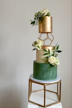 a three tiered cake with gold and green frosting, flowers on each layer