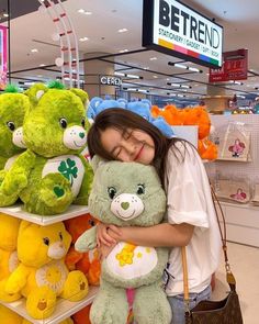 a woman is hugging a large green teddy bear in a store with other stuffed animals behind her