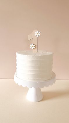 a white cake topped with a single flower on top of a table next to a pink wall