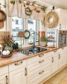 a kitchen decorated for fall with wreaths and greenery on the window sill