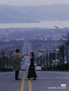 two people standing in the middle of an empty road looking at each other with mountains in the background