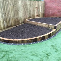 a garden area with raised beds and green grass in the middle, surrounded by a wooden fence