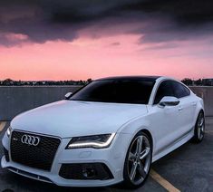 a white car is parked in a parking lot at dusk with the sun setting behind it