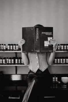 black and white photograph of woman sitting in front of shelves holding up a book