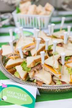 a platter filled with sandwiches and toothpicks on top of a green table cloth