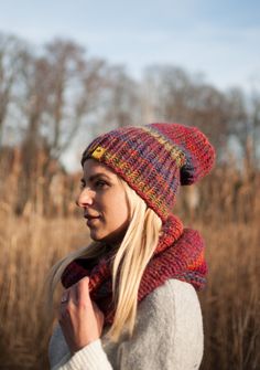 a woman wearing a knitted hat and scarf in a field with tall brown grass