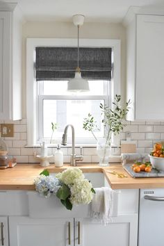 a kitchen with white cabinets and wooden counter tops next to a window filled with flowers