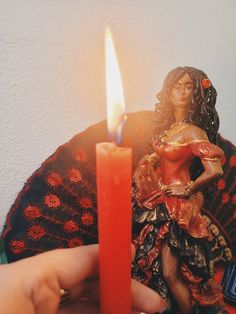 a person holding a lit candle in front of a figurine on a table