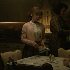 two women standing at a table in a kitchen, one holding a book and the other reading