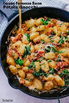 a pan filled with pasta and spinach on top of a blue table cloth next to a wooden spoon