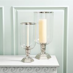 two clear glass candlesticks sitting on top of a white table next to each other