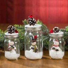 three glass jars with snowmen and pine cones in them