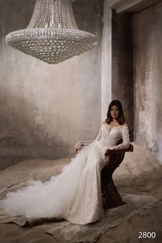 a woman in a wedding dress sitting on a chair with a chandelier hanging from the ceiling